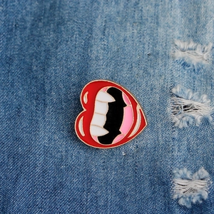 Detail of creative heart-shaped lips and teeth enamel brooch pinned on blue denim fabric