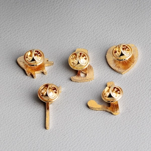 Golden metal brooch set with butterfly clutch pins on a textured leather background
