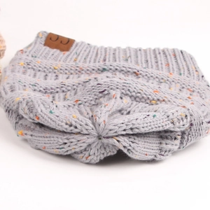 Close-up of light grey confetti knit beanie with a brown leather logo tag detail
