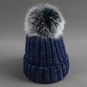 Detail of navy knit beanie with thick ribbing and a large fluffy faux fur pompom on top