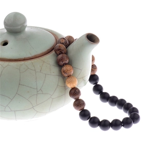 Close-up of black and wood grain beads draped over a vintage celadon teapot