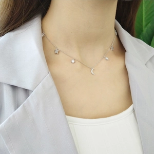 Detailed view of a silver moon and star necklace with zircons on a model's neck