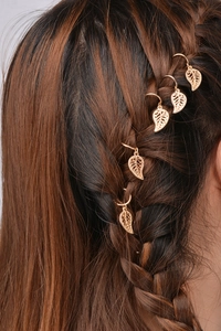 Detail of five golden leaf-shaped metal rings styled on a model's braided hair