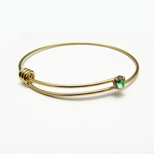 Close-up of golden adjustable wire bangle featuring a knot design and iridescent gemstone