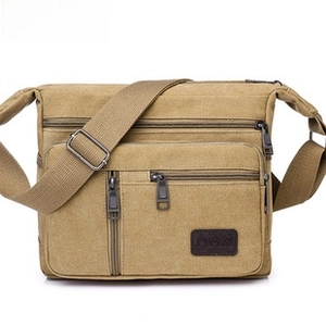 Detail of khaki canvas shoulder bag showing multiple zipper pockets and logo patch