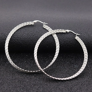 Macro detail of silver hoop earrings featuring an intricate woven texture and secure clasp