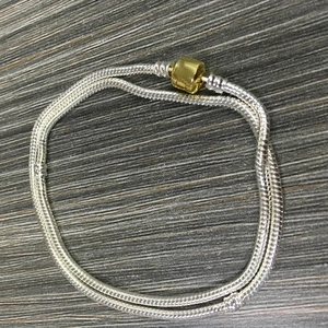 Silver snake chain necklace with golden barrel clasp on grey textured wood background