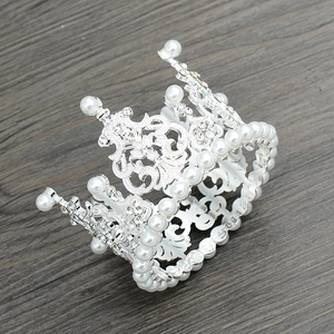 Detail of silver alloy crown with white pearls and rhinestones on dark wood background