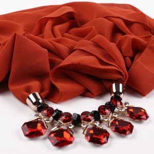 Close-up of caramel chiffon scarf featuring ornate red gemstone and gold metal charms