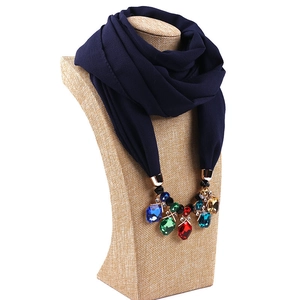 Close-up of navy blue chiffon scarf with colorful gemstone pendant on a display bust
