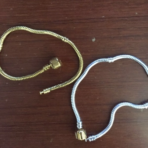 Classic gold and silver snake chain bracelets with barrel clasp on a dark wooden surface