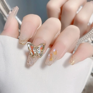 Detalle macro de joyería de mariposa 3D en manicura rosa degradada con purpurina dorada