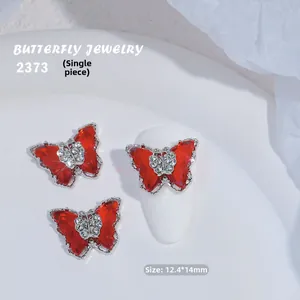 Detalle de adorno de mariposa de circón rojo para uñas con bordes plateados y cristal blanco
