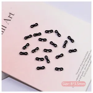 Detail view of black ballet ribbon bowknot nail charms with silver beads on pink background