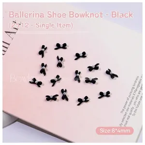 Close-up of matte black bowknot nail charms with white pearl detail for manicure