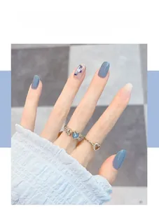 Close-up of golden rings with blue heart gemstones and glittering morandi blue nail art