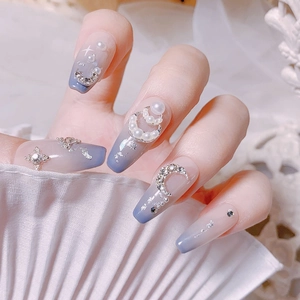 Détail d'ongles dégradés bleus avec lune argentée, perles et strass scintillants
