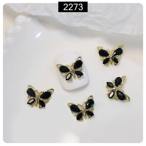 Detail of golden 3D butterfly nail charms with black stones on a white ceramic tray