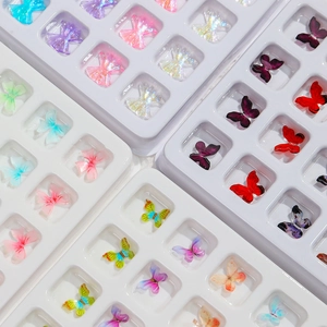 Detailed view of 3D aurora butterfly and bow nail art charms in a white organizer box