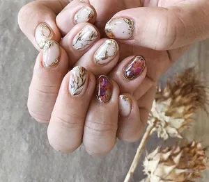 Detailed close-up of cream-colored nail art with gold leaf accents and floral patterns