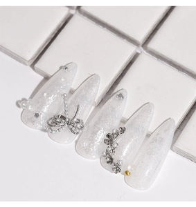Dettaglio di unghie finte bianco perla con fiocchi 3D, strass e accenti di perle