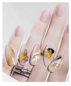 Macro detail of amber marble press-on nails with 3D gold butterfly and purple rhinestones