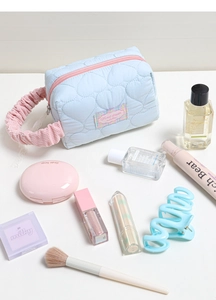 Dettaglio della trousse trapuntata a cuore azzurra con manico rosa e etichetta ricamata