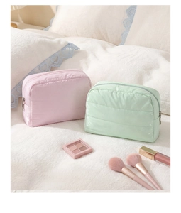 Quilted waterproof cosmetic bags in pink and mint green set on soft white bedding