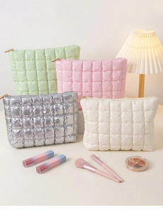 Detailed view of quilted makeup bags in mint green, pink, silver, and cream with gold zippers