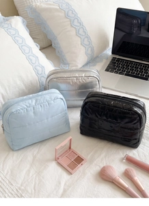 Three quilted down cosmetic bags in blue silver and black colors on a white bed