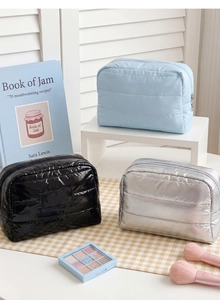 Detailed view of three quilted travel cosmetic bags in blue, gloss black, and silver finish