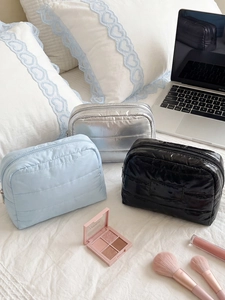 Three-piece set of portable puffer makeup bags in blue, silver, and black on a bed