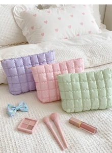 Three quilted makeup bags in lavender, pink, and green colors on a bed setting
