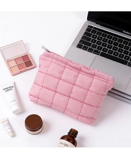 Neceser acolchado rosa con cremallera junto a productos de belleza en un escritorio
