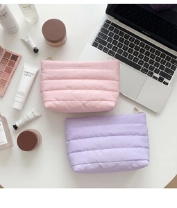 Close-up of quilted puff makeup bags in pink and lilac with gold zipper and stitching