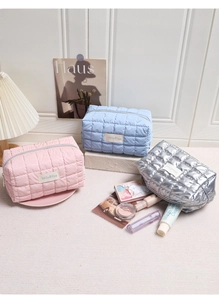 Drie gewatteerde toilettassen in roze, blauw en zilver met accessoires op witte achtergrond