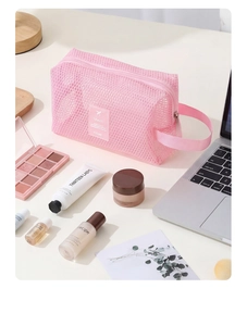 Trousse de maquillage rose en maille avec étiquette de voyage à côté de cosmétiques