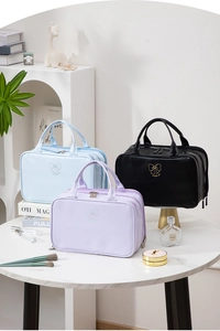 Three multi-compartment travel makeup bags in blue, purple, and black on a marble table