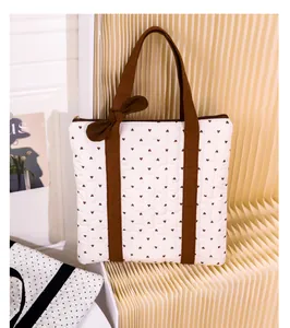 Close-up of white quilted tote bag with brown heart patterns and a decorative bow detail