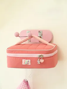 Detailed close-up of pink quilted makeup bag with gold heart and flower zipper charms