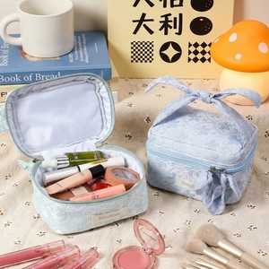 Set of light blue floral lace makeup bags with elegant bow handles on a floral desk