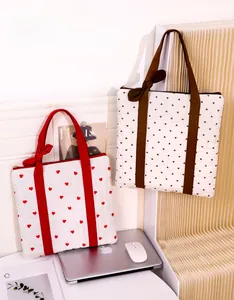 Close-up of quilted heart tote bags with bow details next to a laptop and magazine