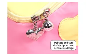 Close-up of dual zippers with silver heart and ball charms on a pink house-shaped makeup bag
