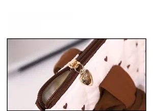 Close-up of golden heart-shaped metal zipper on quilted white bag with brown heart patterns