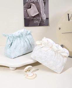 Dettaglio del ricamo floreale in pizzo sulle borse cosmetiche con coulisse azzurre e crema