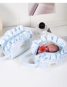Detail of blue checkered makeup bag featuring elegant ruffle trim and side brand label