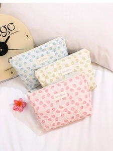 Detailed view of floral lace makeup bags with metal zipper and brand label on white bedding