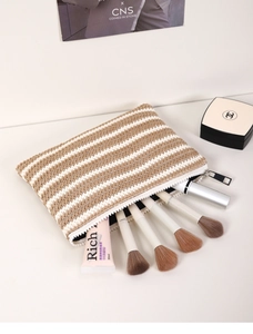 Detail of striped woven makeup bag featuring brushes and interior lining on white background