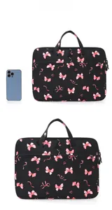 Close-up of black laptop bag with pink bow pattern and top handle next to phone for scale
