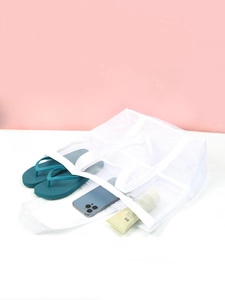 Close-up of white mesh beach bag holding flip-flops and phone on pink background